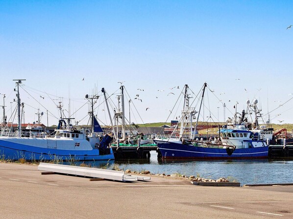 A marina with multiple fishing boats docked, a clear sky, and a calm water surface.