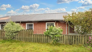 A brick house with a tiled roof, a wooden fence, and a grassy yard.