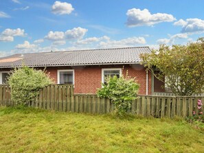 A brick house with a tiled roof, a wooden fence, and a grassy yard. - 8 Person Holiday Home in Hvide Sande (Hvide Sande)