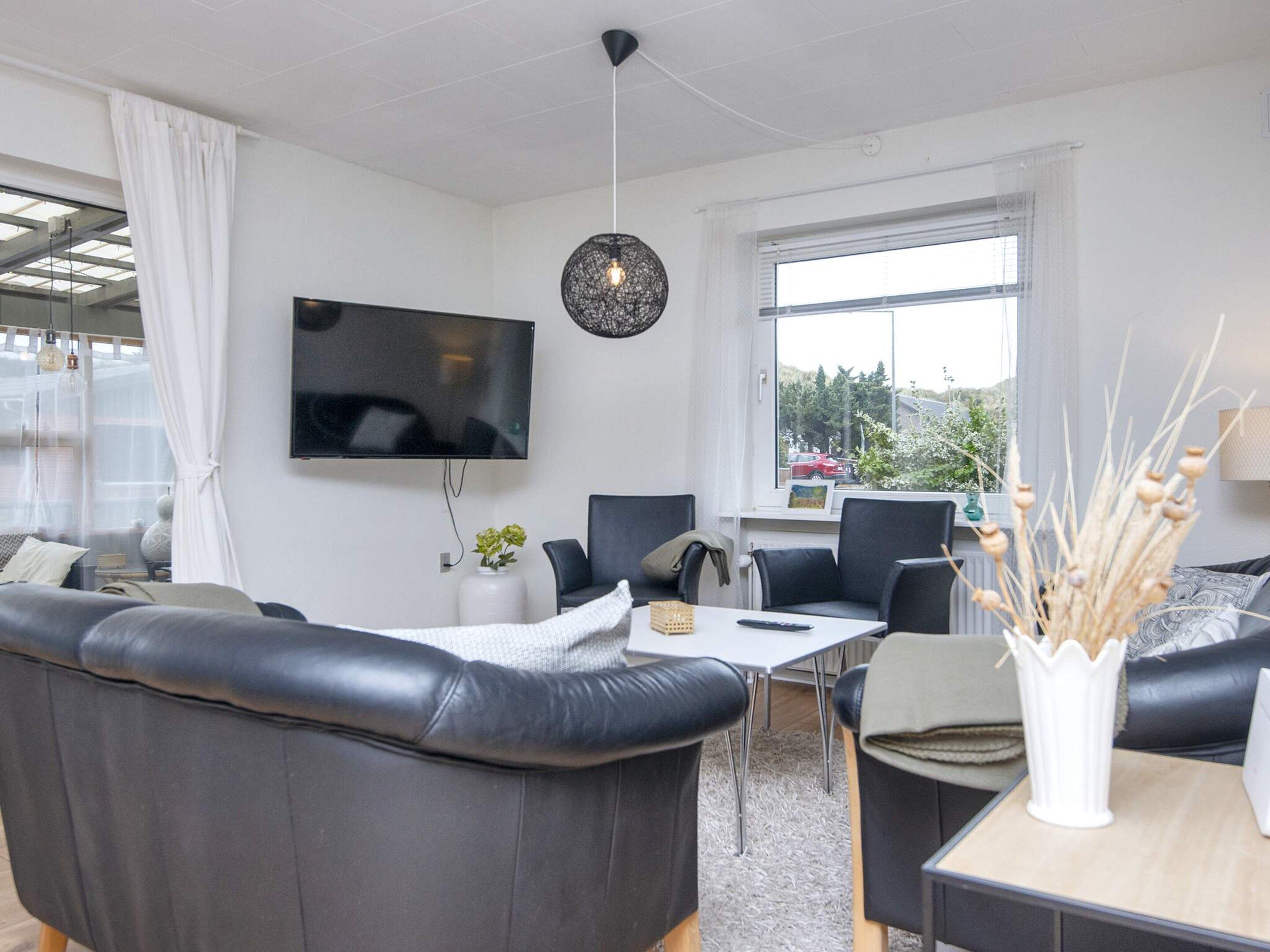 Un salon moderne avec un canapé en cuir noir, un téléviseur à écran plat fixé au mur et un coin repas comprenant une table et des chaises.