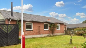 Une maison en briques avec un toit en tuiles, une cour clôturée et un ciel dégagé.