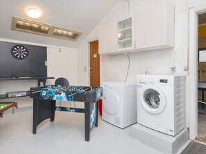 A room with a foosball table, a dartboard, a washing machine, and a cabinet with glass doors.