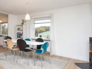 A modern kitchen with a dining area, white walls, and a view of greenery outside.