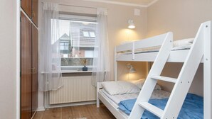 Une chambre avec un lit superposé, une fenêtre, un radiateur et un petit tapis.