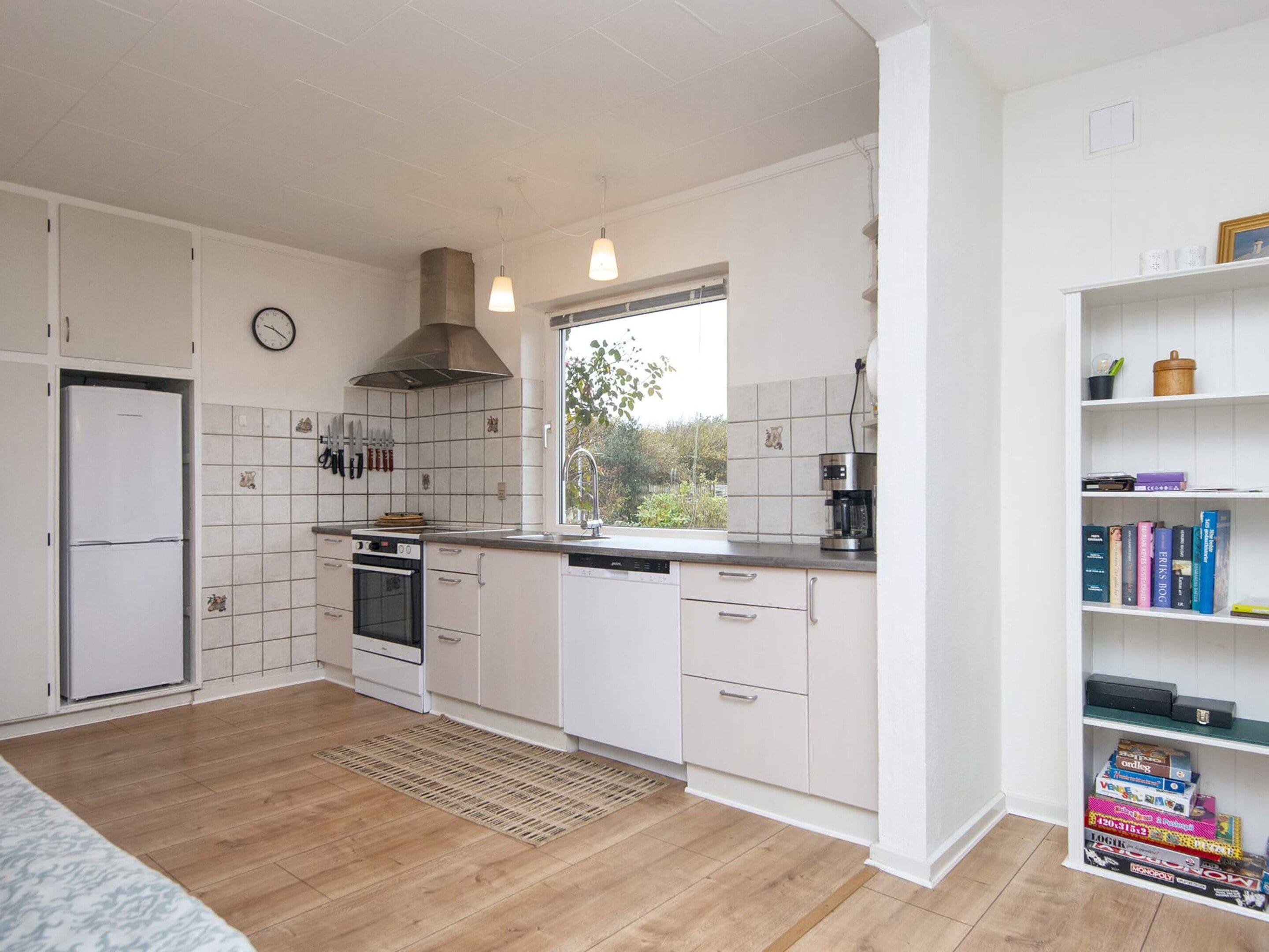 A modern kitchen with white cabinetry, a built-in oven, a coffee maker, and a window with a view of greenery.