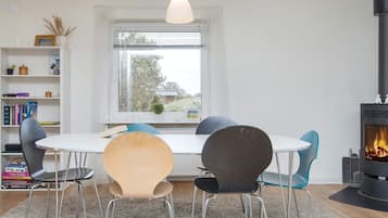 A modern dining area with a white table, four chairs, a hanging light fixture, a bookshelf, and a fireplace.