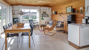 A cozy cabin interior with a wooden ceiling, a dining area with a table and chairs, a seating area with a sofa and chairs, a kitchenette with appliances, and a television. - 4 Person Holiday Home in Vaeggerlose (Vaeggerlose)
