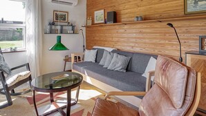 A cozy living room with a wooden ceiling, a grey sofa, a glass coffee table, and a leather armchair. - 4 Person Holiday Home in Vaeggerlose (Vaeggerlose)