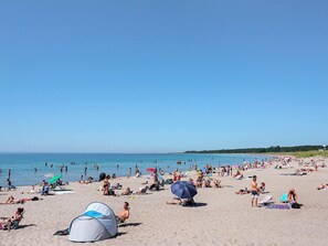 A crowded beach with people sunbathing, swimming, and using umbrellas.