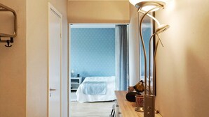 Quarto de hotel com uma cama, uma escrivaninha com luminária, uma cadeira e vista para outro quarto.