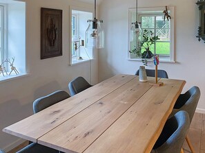 A dining area with a wooden table, chairs, pendant lights, and a window with a view of greenery. - 6 Person Holiday Home in Varde (Varde)