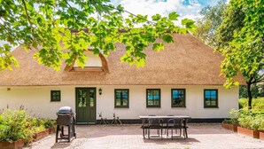 A thatched-roof house with a paved patio, a barbecue grill, and a table with chairs. - 6 Person Holiday Home in Varde (Varde)