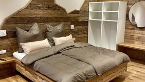 A bedroom with a wooden headboard, a bed with grey bedding, a white wardrobe, and a bedside table with a lamp.