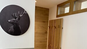 A hallway with a wooden floor, a circular wall art of a deer, a wooden panel wall, and a window with a wooden frame.