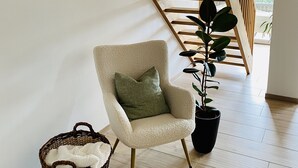 A modern interior with a wooden staircase, a plush armchair, a potted plant, and a wicker basket.