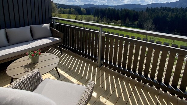 A wooden deck with a sofa and wicker chairs, overlooking a mountainous landscape.