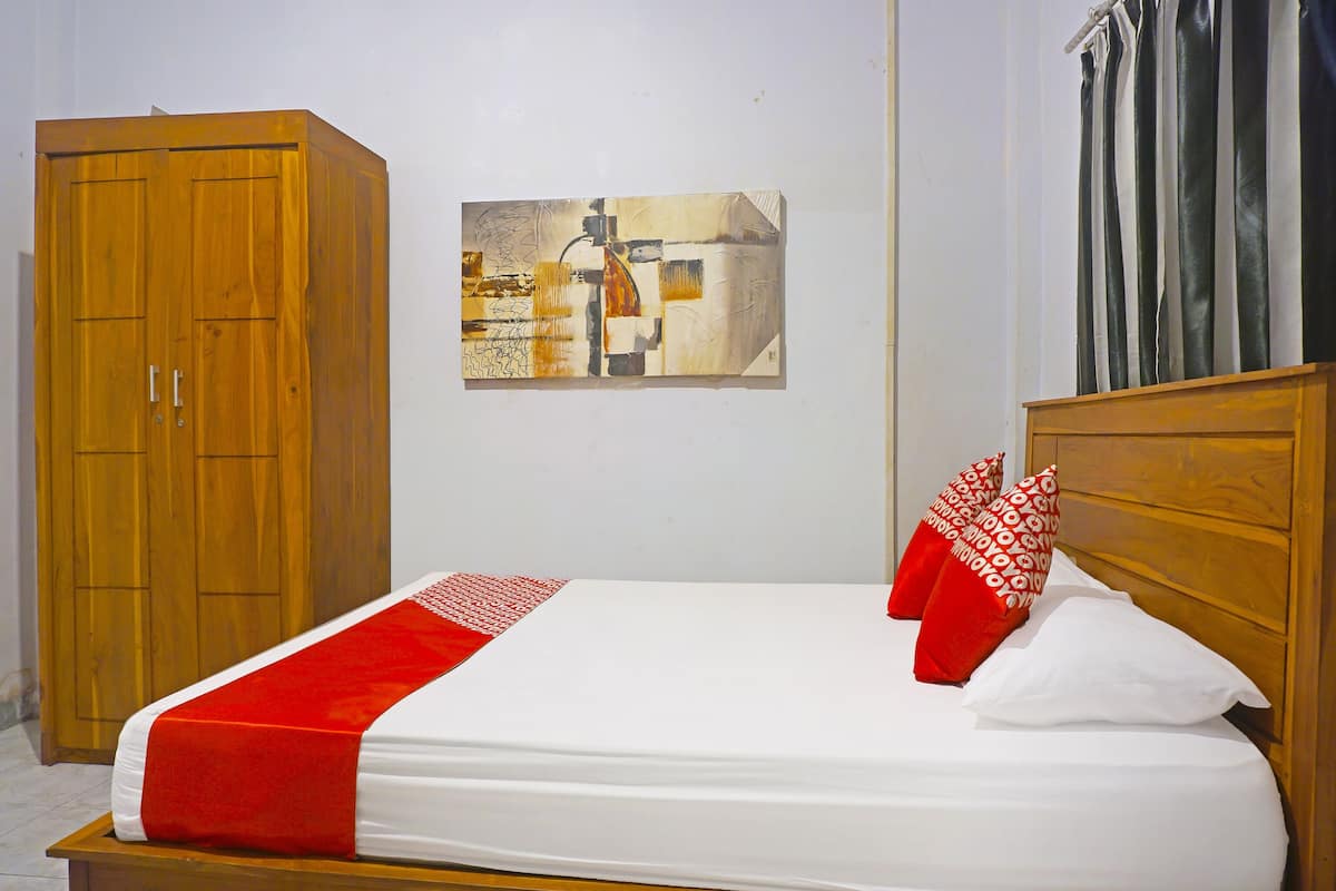 A neatly made bed with a red and white bedspread, a wooden headboard, and a wall-mounted painting.