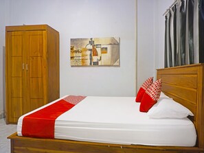 Cama bem arrumada com colcha vermelha e branca, cabeceira de madeira e um quadro pendurado na parede.