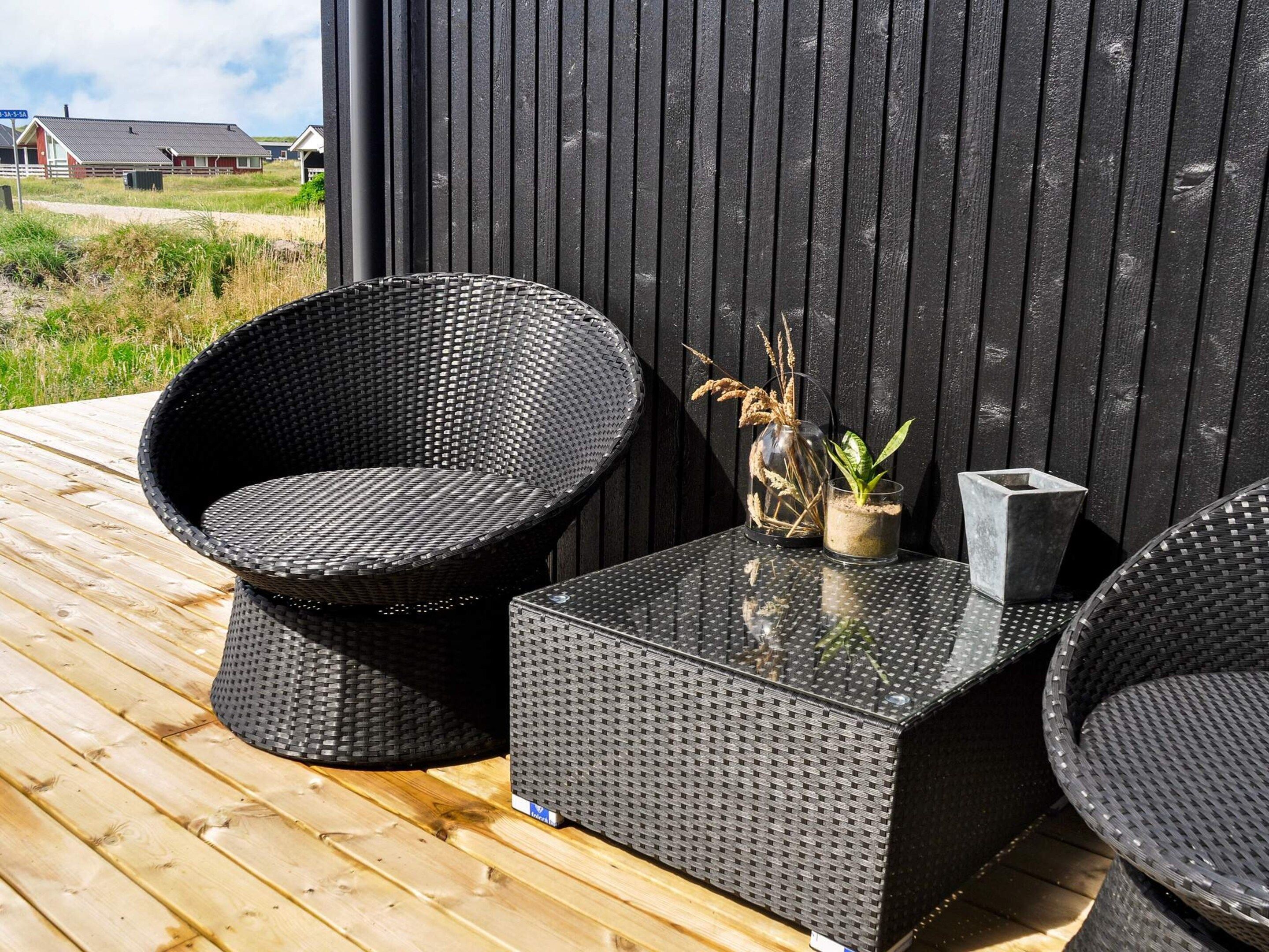 A deck with two black wicker chairs and a matching table, a glass vase with dried plants, and a stone planter.