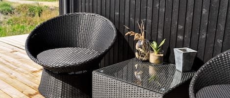 En terrasse med to sorte fletstole og et tilhørende bord, en glasvase med tørrede planter og en stenplanter.