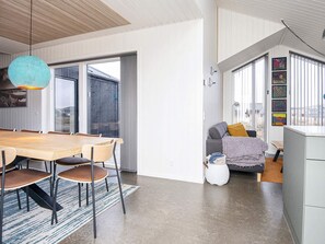A modern kitchen with a dining table and chairs, a sofa, and a large window with artwork. - 5 Star Holiday Home in Harboore (Harboore)