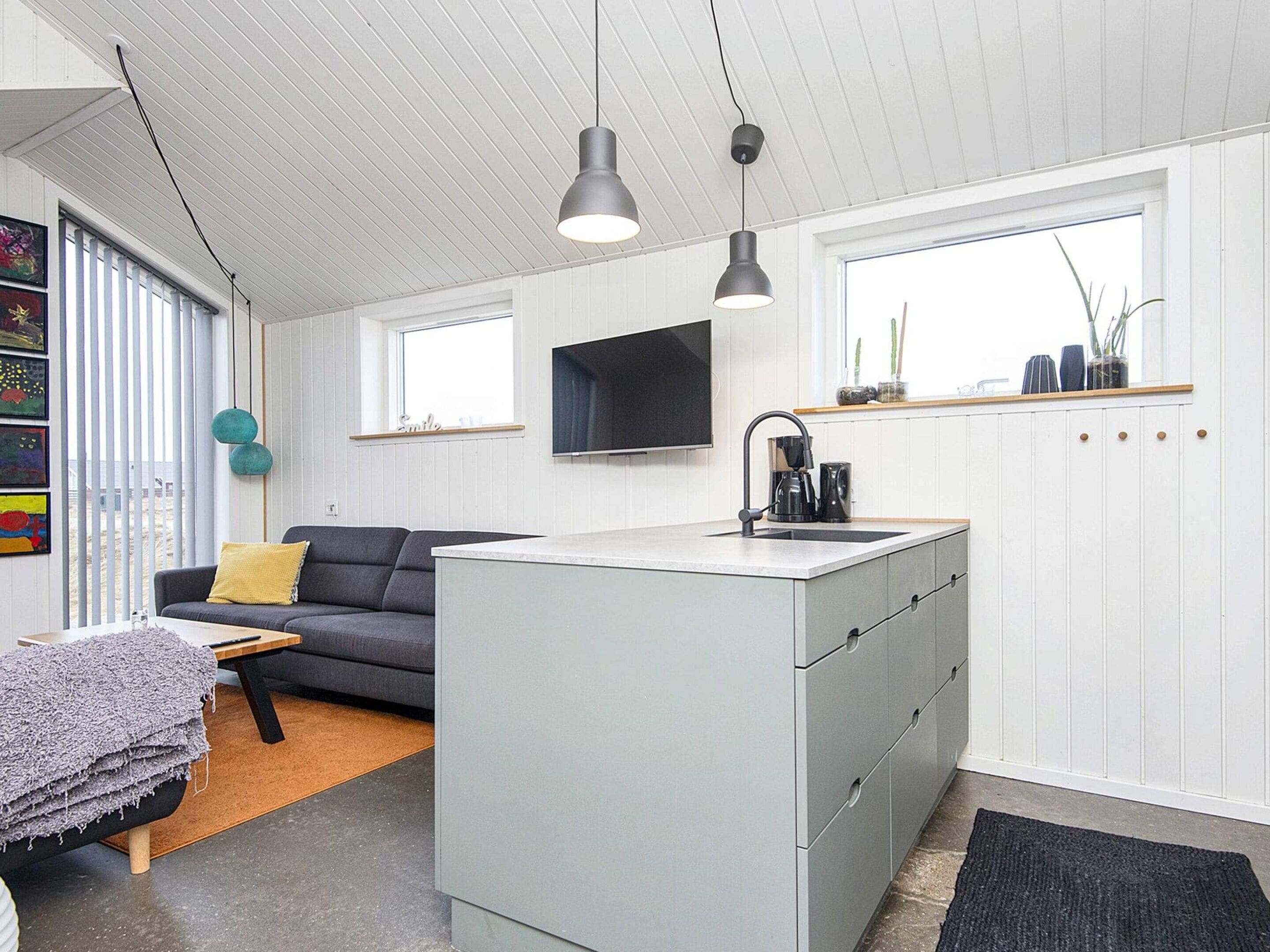 A compact living space with a kitchenette, a sofa, a coffee table, and a television mounted on the wall.