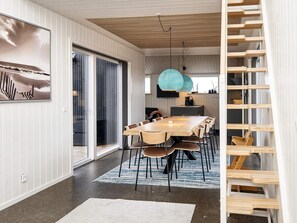 A modern dining area with a wooden table and chairs, a large pendant light, and a view of the outdoors through a sliding glass door.
