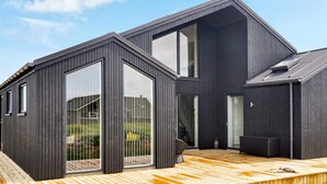 Ett modernt hus i två våningar med stora fönster och en träveranda.