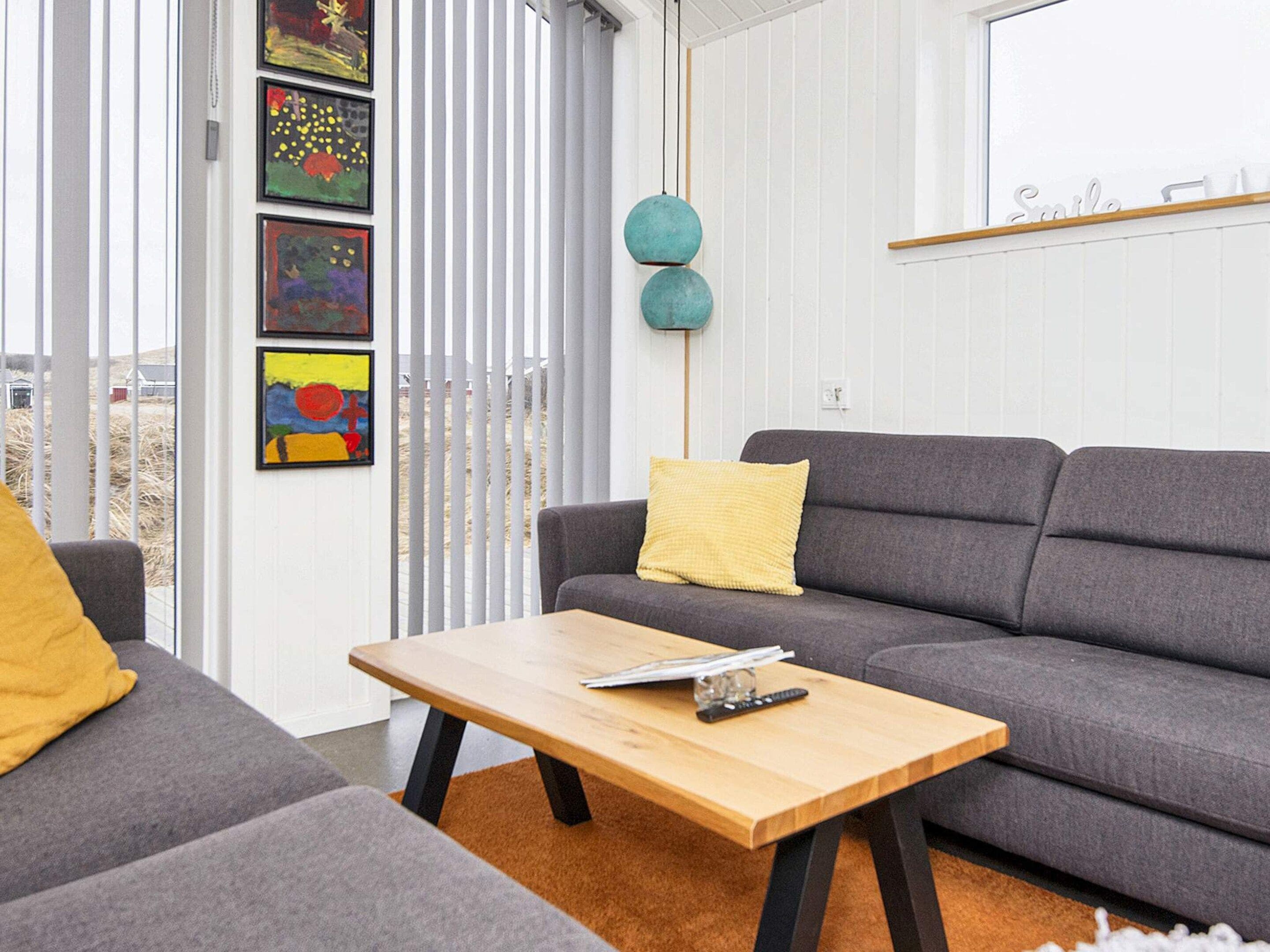 Ein modernes Wohnzimmer mit einem grauen Sofa, einem Holztisch und einem gelben Kissen.