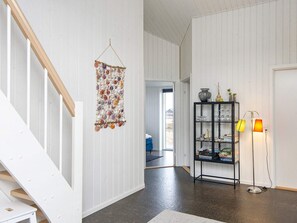 A hallway with a wooden staircase, a wall-mounted decorative item, a glass cabinet with items, and a floor lamp.