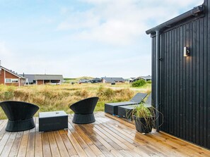 A wooden deck with outdoor furniture, a black building, and a view of houses in the background. - 5 Star Holiday Home in Harboore (Harboore)
