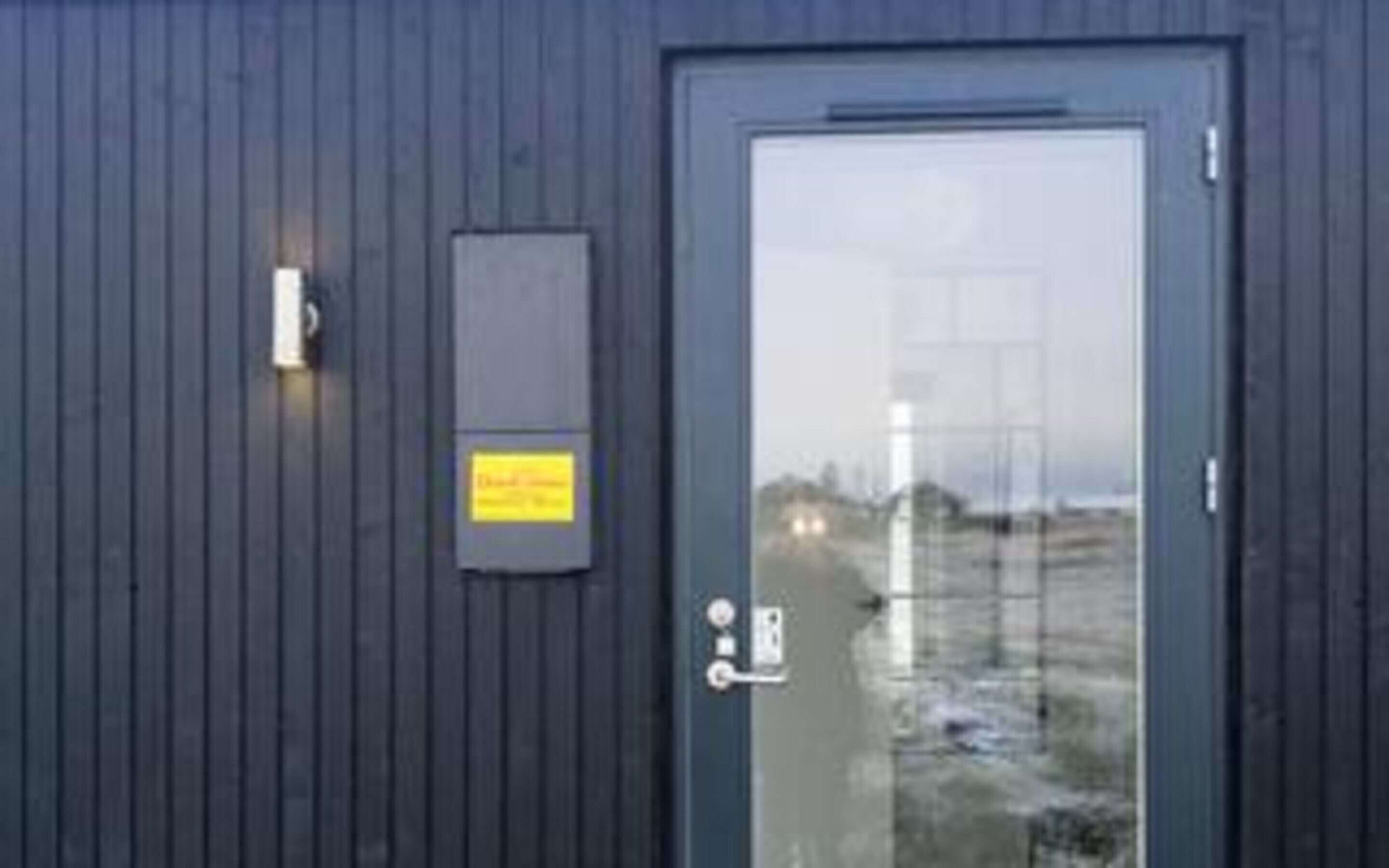 A dark wooden door with a glass panel, a small yellow sign, and a keypad lock.
