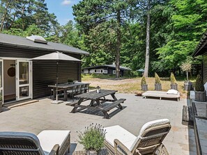 An outdoor patio area with a wooden table and chairs, a barbecue grill, and a covered seating area.