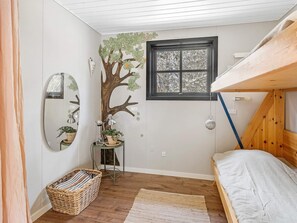 A bedroom with a bunk bed, a mirror, a small table with plants, a window, and a wooden floor.
