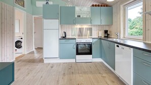 A modern kitchen with light blue cabinets, a white refrigerator, a stove, and a sink. There is a window providing natural light and a view of greenery outside. - 6 Person Holiday Home in Nykobing Sj (Nykobing Sjaelland)