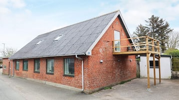 A red brick building with a sloped roof, a wooden deck, and a small window.