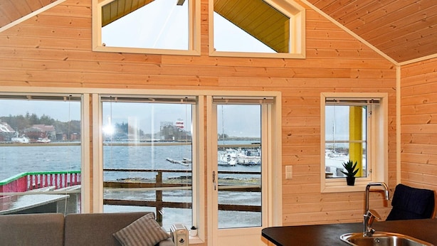 A cozy cabin with a wooden interior, a sofa, a dining area, and a view of a frozen body of water.