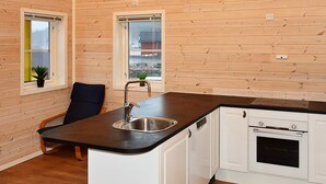 A compact kitchen with wooden walls, a black countertop, a sink, a dishwasher, and a stove.