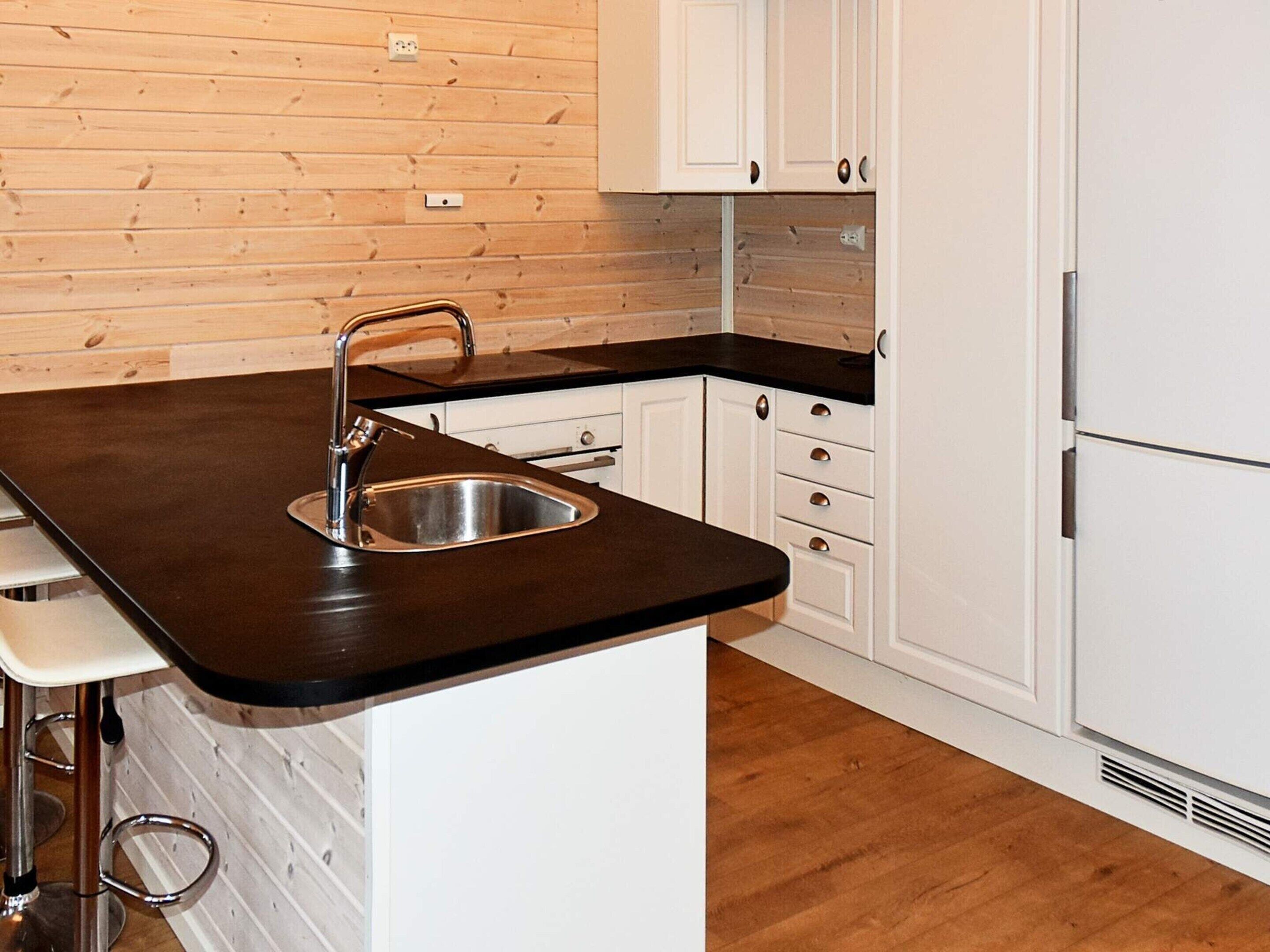 A kitchen with a black countertop, stainless steel sink, white cabinets, and a wooden wall.