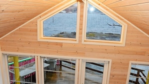 A room with a sloped wooden ceiling, large windows, and a view of a body of water.