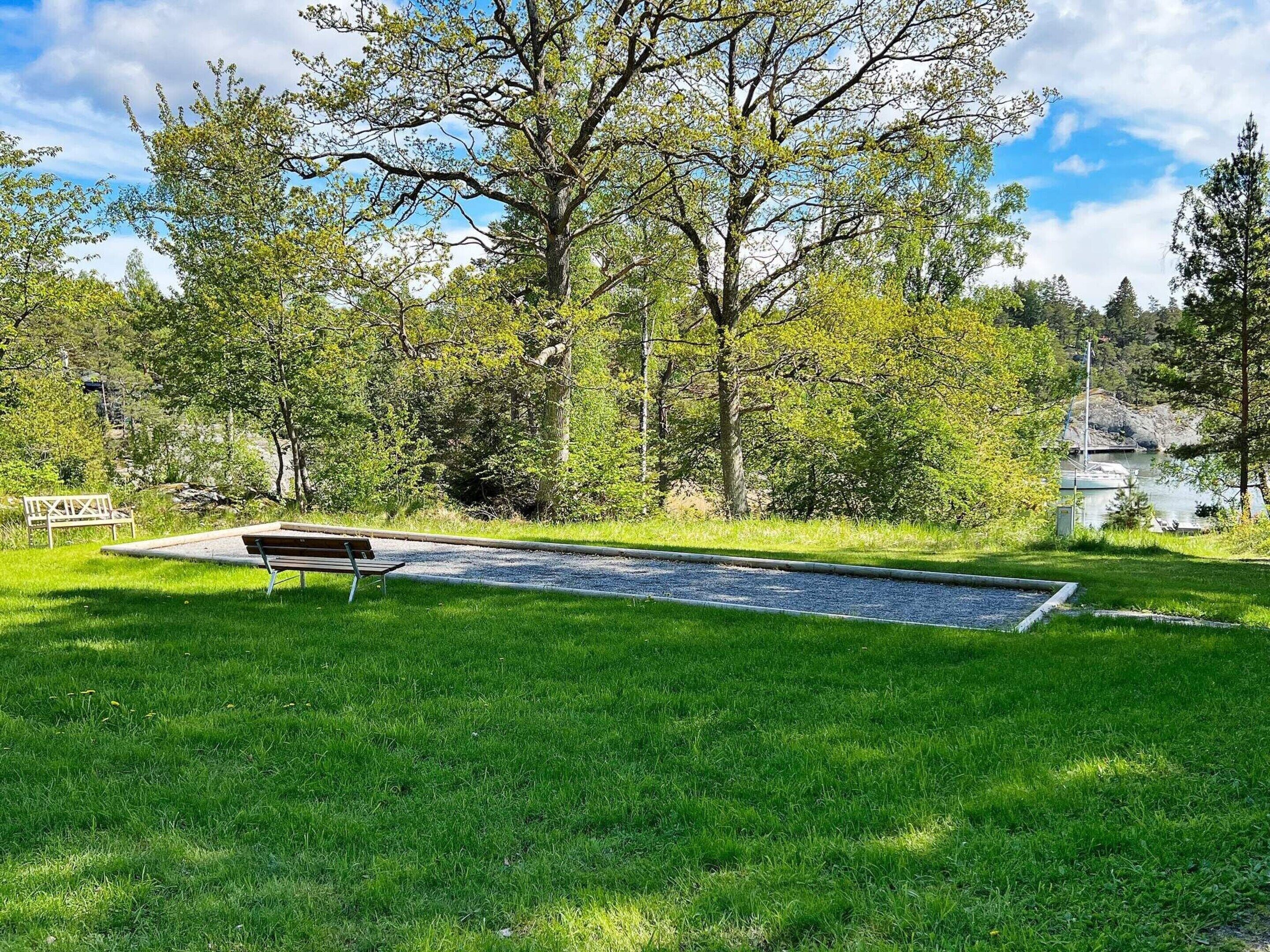 A park with a bench, a paved area, and a lake in the background.
