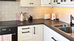 Una cocina con armarios blancos, encimera negra, pileta de acero inoxidable y campana extractora negra.
