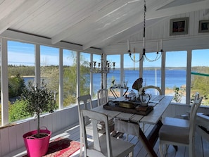 A covered porch with a table and chairs, a potted plant, and a view of a lake.