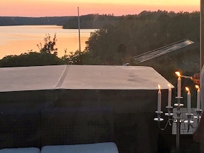 A rooftop with a view of a lake at sunset, a covered outdoor seating area, and a candelabra with lit candles.