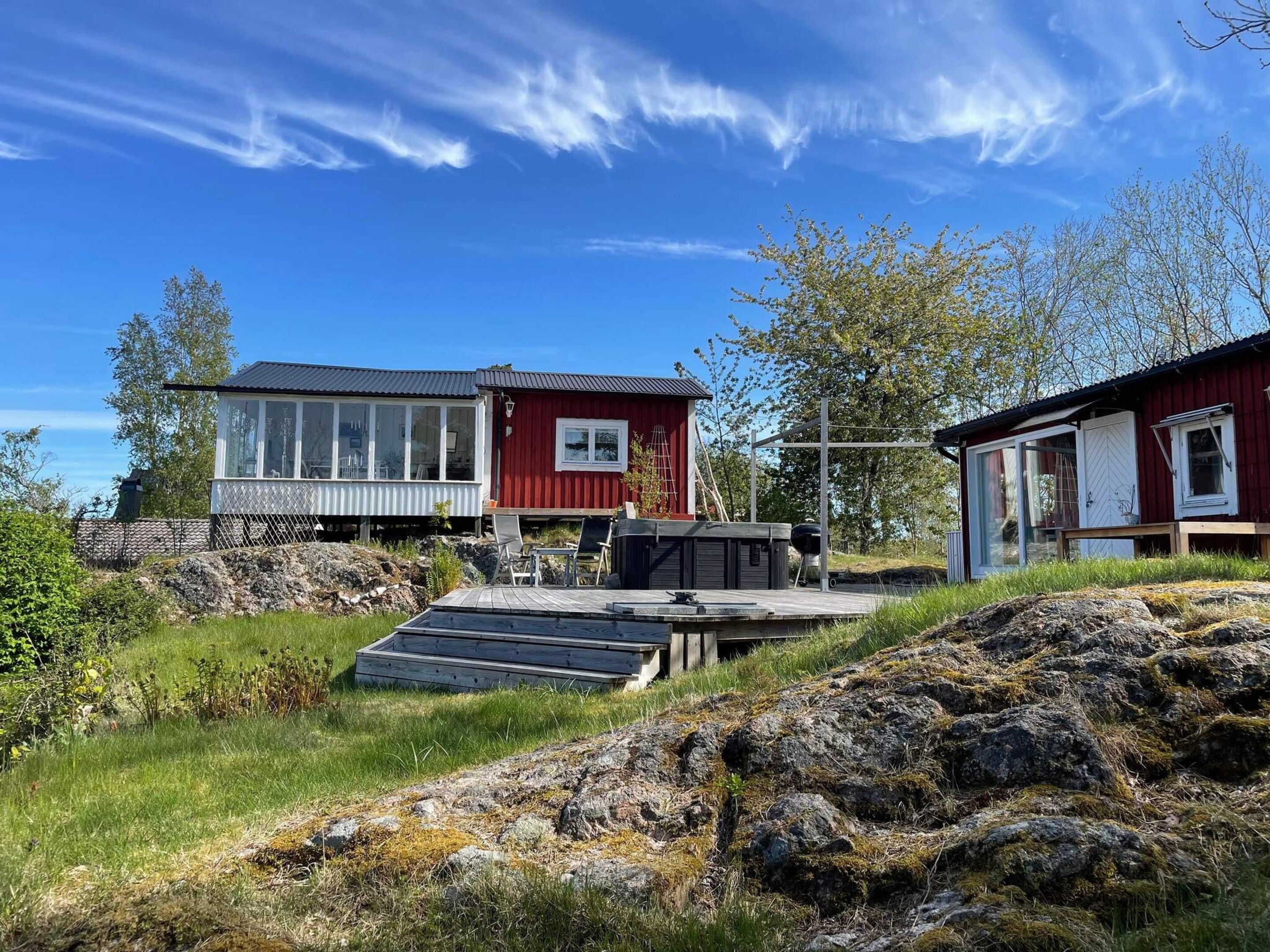 A red cabin with a glass extension, a deck, and a small outdoor seating area.