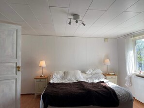 A bedroom with a bed, two bedside lamps, a window with curtains, and a ceiling light fixture.