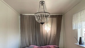 A bedroom with a bed, a chandelier, curtains, and a window with a view.