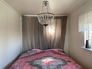 A bedroom with a bed, a chandelier, curtains, and a window with a view.