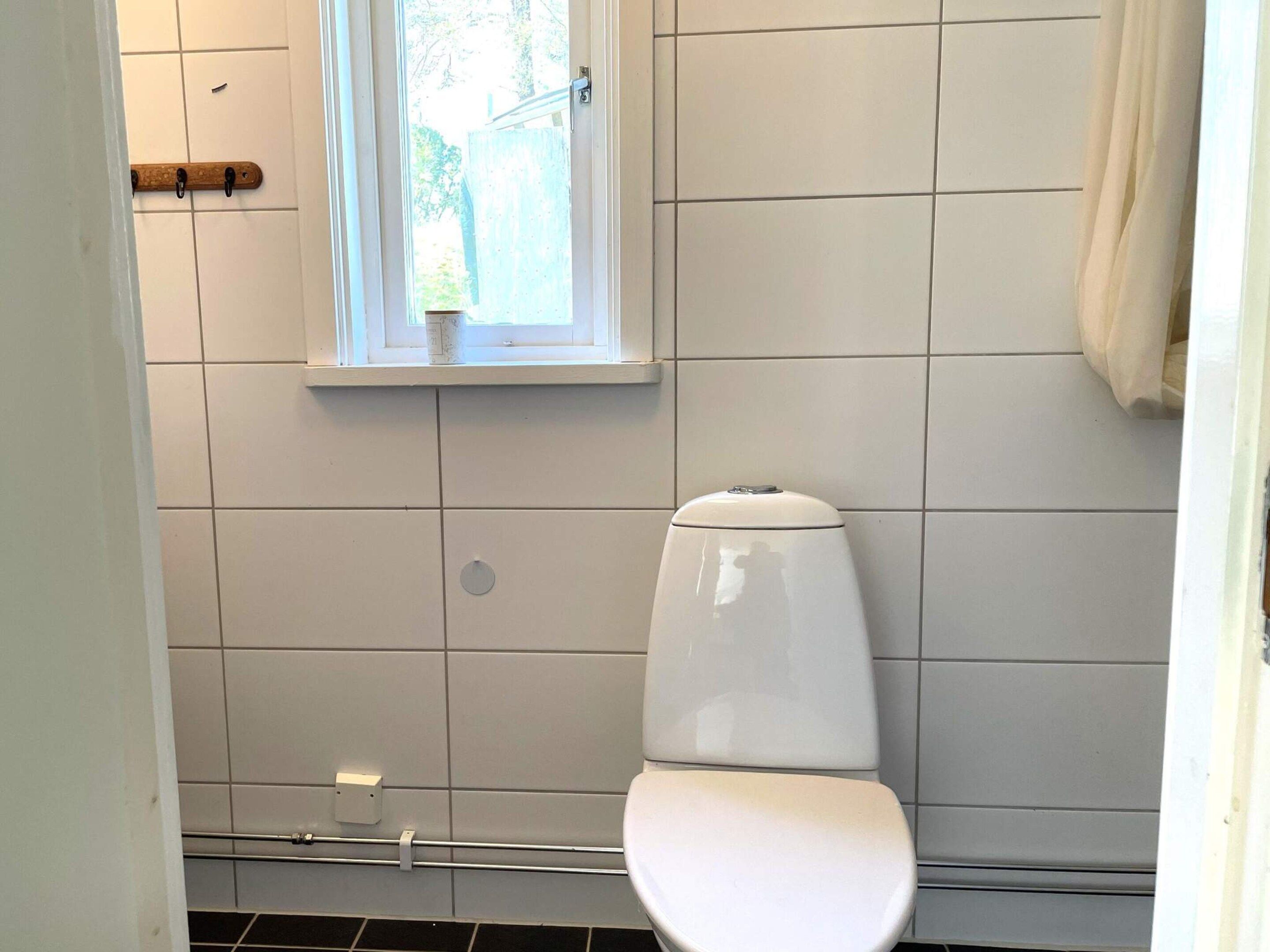 A bathroom with white tiles, a toilet, a window, and a towel rack.