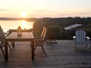A wooden deck with a table and chairs, overlooking a body of water at sunset. - 4 Star Holiday Home in Trollhattan (Trollhattan)
